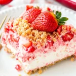 A slice of strawberry crunch cake with fresh strawberries and crumbled topping on a plate, with a fork beside it.