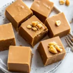 Peanut butter fudge squares topped with crushed peanuts, served on a plate with a fork.